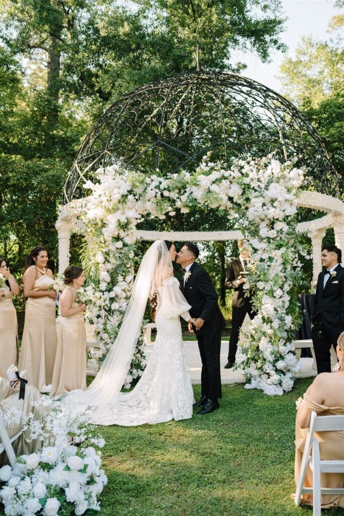 green-white-spring-wedding-chateau-nouvelle-venue-outdoor-ceremony-AVP-ashleys-visions-productions-houston-wedding-planner-ceremony-couple-kiss-floral arch